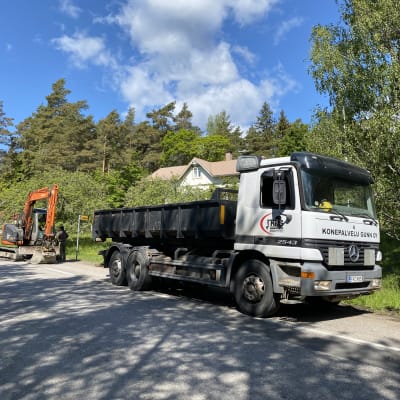 En grävmaskin och lastbil vid en vägren.