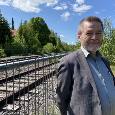 Suomen Lähijuna Oy:n johtohahmo Antero Alku katsoo kameraan junaradan varrella ja hymyilee.