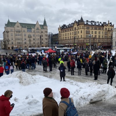 Mielenosoittajia Tampereen keskustorilla. Kuva kaukaa ihmisjoukosta, taustalla näkyy Hämeenkatu. Torilla on paljon lunta. 