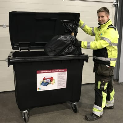 En man sätter en påse med avlagda textilier i en soptunna för det ändamålet.