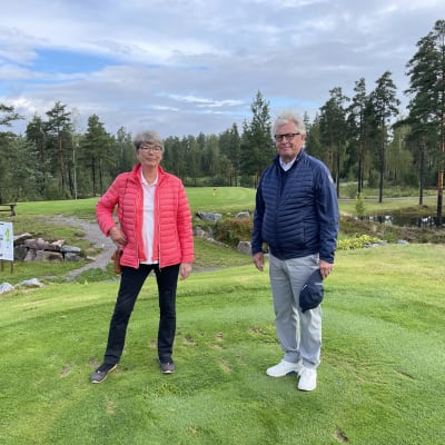 Porträtt av Annika Colérus och Henrik Sarajas som står bredvid varandra och ser in i kameran. De står på en golfbana, i bakgrudnen finns terränghinder. 