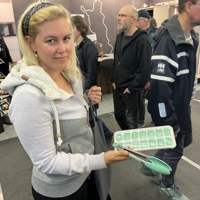 Nainen messujen ihmisruuhkassa esittelee silikoonista valmistettuja keittiövälineitä.