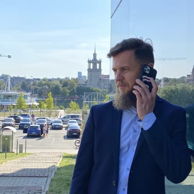 Man med blå kostym och ljusblå skjorta talar i mobiltelefon utanför ett konferenshotell i Vilnius. Mannens mobiltelefon pryds av Belarus rödvita oppositionsflagga.