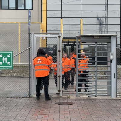 Teräasaita varaston edessä, portti ja ihmisiä portin lähettyvillä