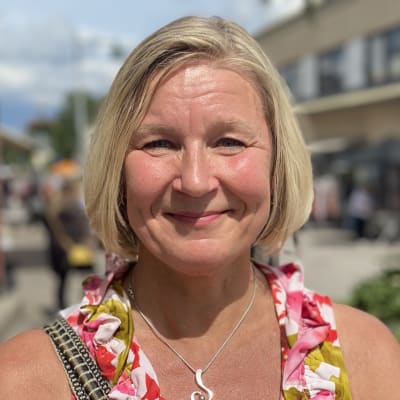 Glad kvinna i färgglad klänning står på gata i Pargas i solsken. 