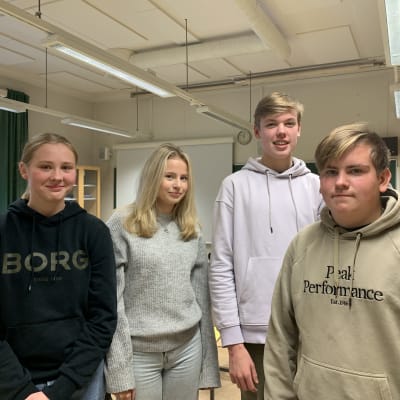 En grupp på fyra skolelever poserar på bild i klassrum, de är alla tonåringar, till vänster står två flickor och till höger två pojkar.