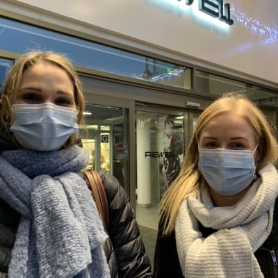 Två kvinnor med munskydd står utanför ingång till köpcentrum.