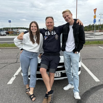 Laura Törnroos och Niklas Grönholm står vid en bil tillsammans med bilskolläraren Johan Hurmerinta.