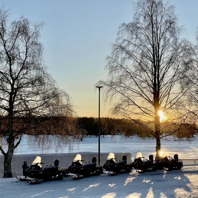 Moottorikelkkoja rivissä, taustalla kerrostalo, johon osuu auringonvalo.
