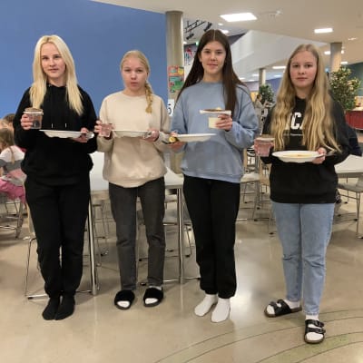 Neljä nuorta seisoo lautasten kanssa ilman tarjottimia.