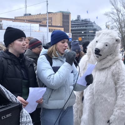 En demonstrant talar i mikrofon med en person i isbjörnsdräkt bredvid sig.