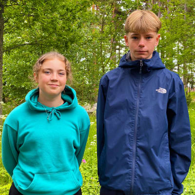 Amanda Ertiö och Dennis Albrecht står bredvid varandra och tittar in i kameran. De är båda iklädda blått och står framför ett grönskande område.