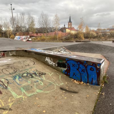 En skateboardramp och andra skateboardredskap på en asfaltsplan. I bakgrunden syns Lovisa kyrka och andra hus.