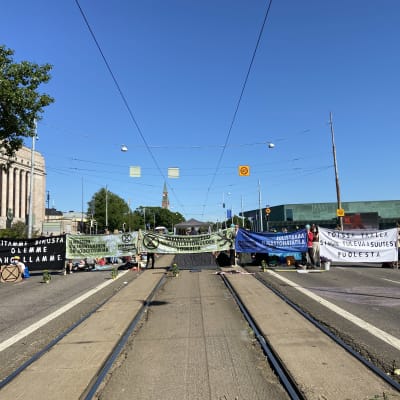 Demonstranter står med plakat på Mannerheimgatan vid riksdagshuset
