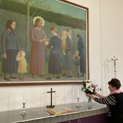 Nainen asettelee kukkasia maljakkoon Kitinojan kirkon alttarilla.