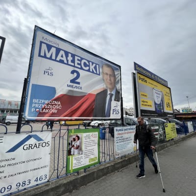 En man på kryckor går framför en valaffisch i Polen