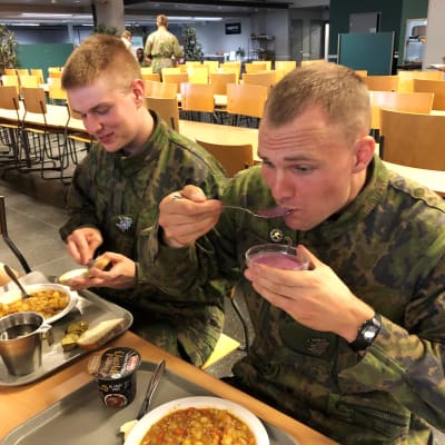 Jääkäri Saku Putkonen näyttää, miten nopeasti armeijassa syödään.  Jääkäri Mitja Risku myhäilee taustalla.