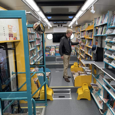 Kirjastoautonkuljettaja Jarmo Lähteenmäki laittaa kirjaa hyllyyn sinisen ja keltaisen värisessä kirjastoautossa