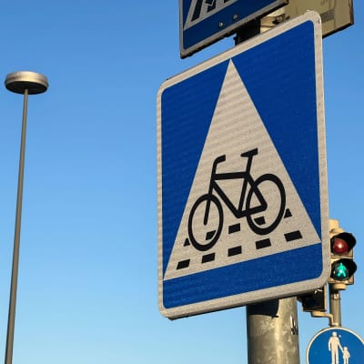 Liikennemerkki B7, väistämisvelvollisuus pyöräilijän tienylityspaikassa. Neliönmallisessa sinipohjaisessa merkissa on valkoisen kolmion sisällä polkupyörän kuva sekä katkoviivoitus osoittamassa pyörätien jatketta.