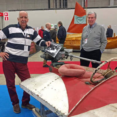 Nisse Häggblom och en annan Nisse står intill en gammal racingbåt i faner från 30-talet