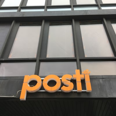 Postens orangea logo på en dyster mörk fasad.