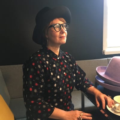 Designern Hanna Sarén sitter på ett café med hattar på bordet.