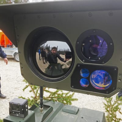 Yles medarbetare Gustaf Antell syns i spegelbilden på en detalj av en kulspruta monterad på ett obemannad bandvagn.