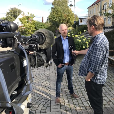 Svt-journalist intervjuar André af Geijerstam framför tv-kamera intill Sjöbo kommunhus.