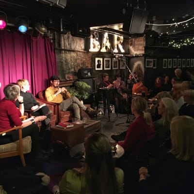 En panel med författare sitter på en upplyst scen i en fullsatt källarlokal.