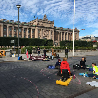 Demonstranter sitter på gata och bro utanför riksdagshuset i Stockholm.