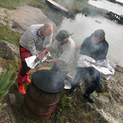 Ove Englund, Matias Jungar och Michael Björklund står och plockar ut fisk ur en rökugn.