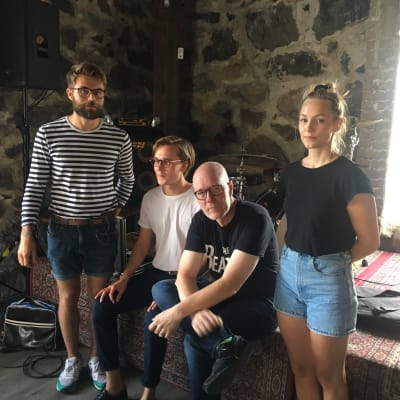 bandmedlemmar i she's leaving home poserar med allvarliga miner framför deras instrument med en stenvägg i bakgrunden