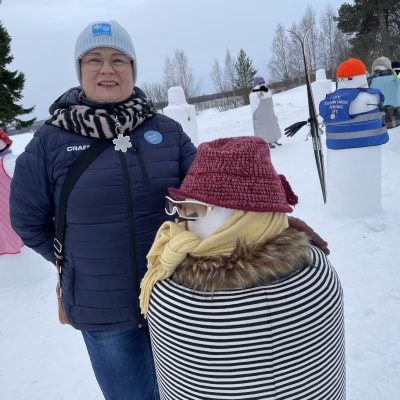 Kemijärven matkailusihteeri Ann-Christine Lampela seisoo tyytyväisenä Kemijärven kulttuurikeskuksen pihalla. Takana häämöttää Pöyliöjärvi. Vieressä ehta aito kemijärveläisestä lumesta tehty lumihenkilö.