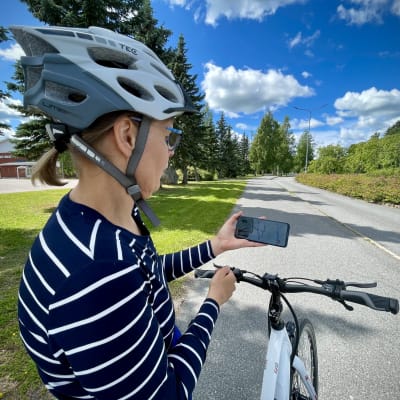 Loimaan kaupungin palvelusihteeri Heli Koivisto seisoo polkupyöränsä vieressä ja tutkii puhelimen näytöltä Crowdsorsa-mobiilipeliä.