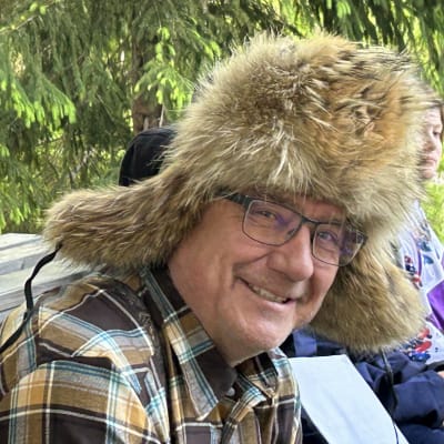 Karvalakkipäinen hymyilevä mies katsoo suoraan kameraan.