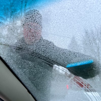 Mies skrapaa auton tuulilasia lumesta.