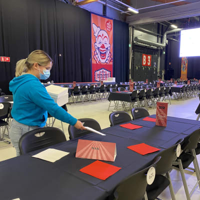 Nainen laittaa papereita pöydälle Jyväskylän Paviljongissa. Pitkiä pöytiä on paljon.