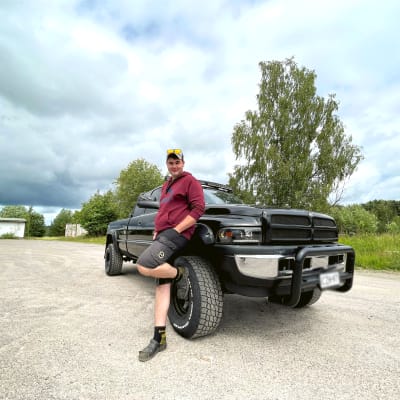 En man står och lutar mot en svart flakbil.