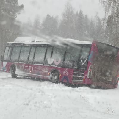 En buss som sladdat i snöyran och lagt sig tvärs över vägen med bakre delen i diket. 