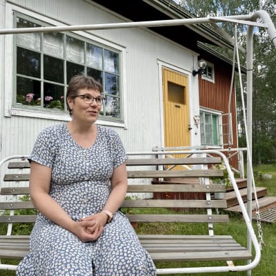 Hyrynsalmelle vanhaan mummolataloonsa muuttanut Katja Kuismin-Jokinen istumassa talon edustalla pihakeinussa.