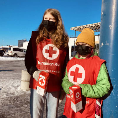 Kaksi lasta pitelee Punaisen Ristin keräyslippaita käsissään.