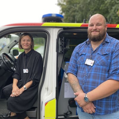 Kvinna sitter i ambulans, man står framför fordonet