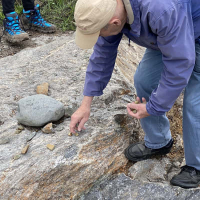 En sten med text på ligger på berggrunden. En man plockar upp små stenar.