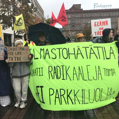 Elokapinan jäseniä kylttien kanssa Tampereen keskustassa. Kylteissä lukee muun muassa "Ilmastohätätila vaatii radikaaleja toimia, ei parkkiluolia."