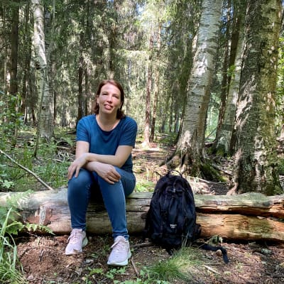 Nina Karisalo istuu puun rungolla Matokallion metsässä. 