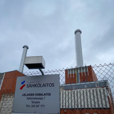 Tampereen Sähkölaitoksen Lielahden voimalaitos kuvattuna ulkoapäin. Tiilistä rakennettu, massiivinen laitos, josta nousee useampi korkea piippu. Taustalla pilvinen taivas.