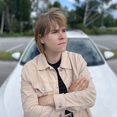 Sofia Tawast nojaa valkoiseen autoon kädet puuskassa. 