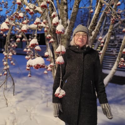 Nainen seisoo talvivaatteissaan lumisen pihlajan katveessa.