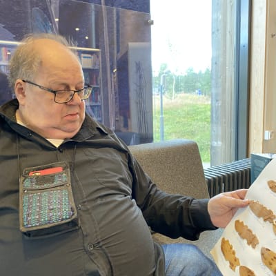 Mies istuu sohvalla poromerkkitaulu kädessään.