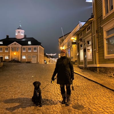 Barbro står på rådhustorget i Borgå med sin svarta hund.